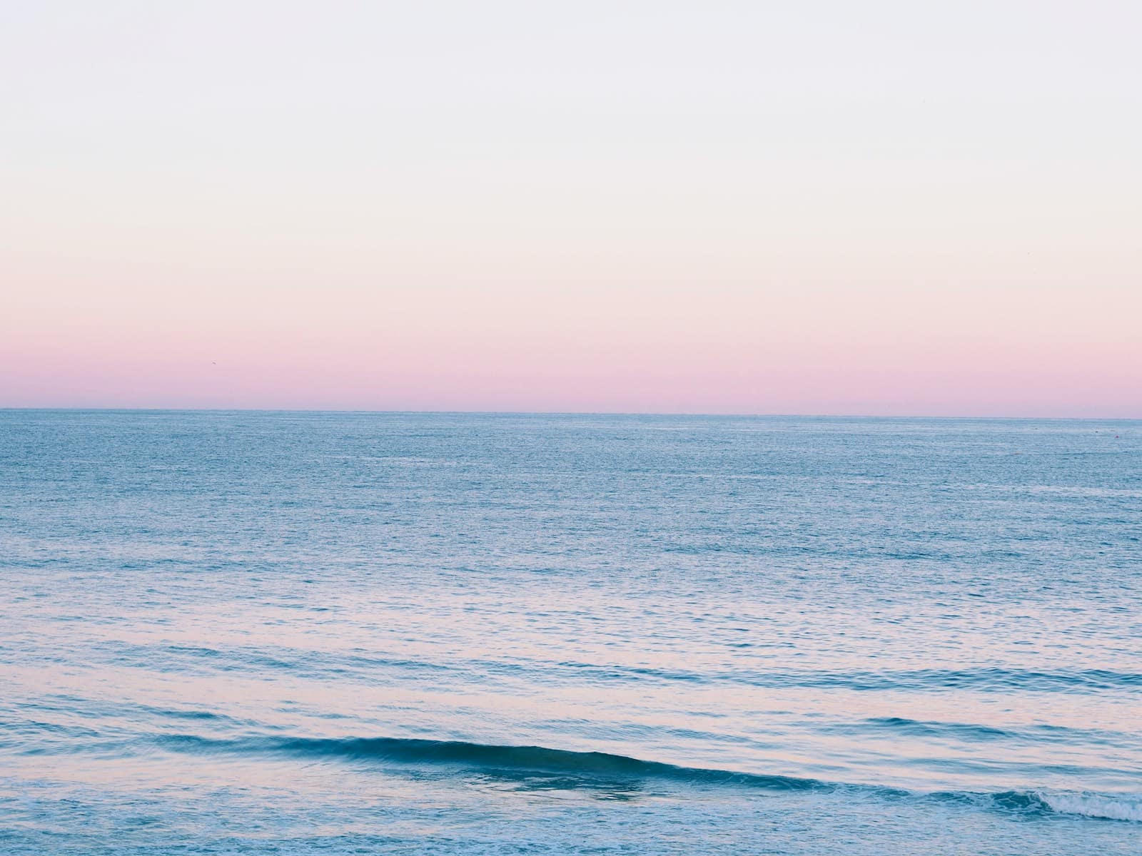 A calm ocean under a soft pink sky at dusk