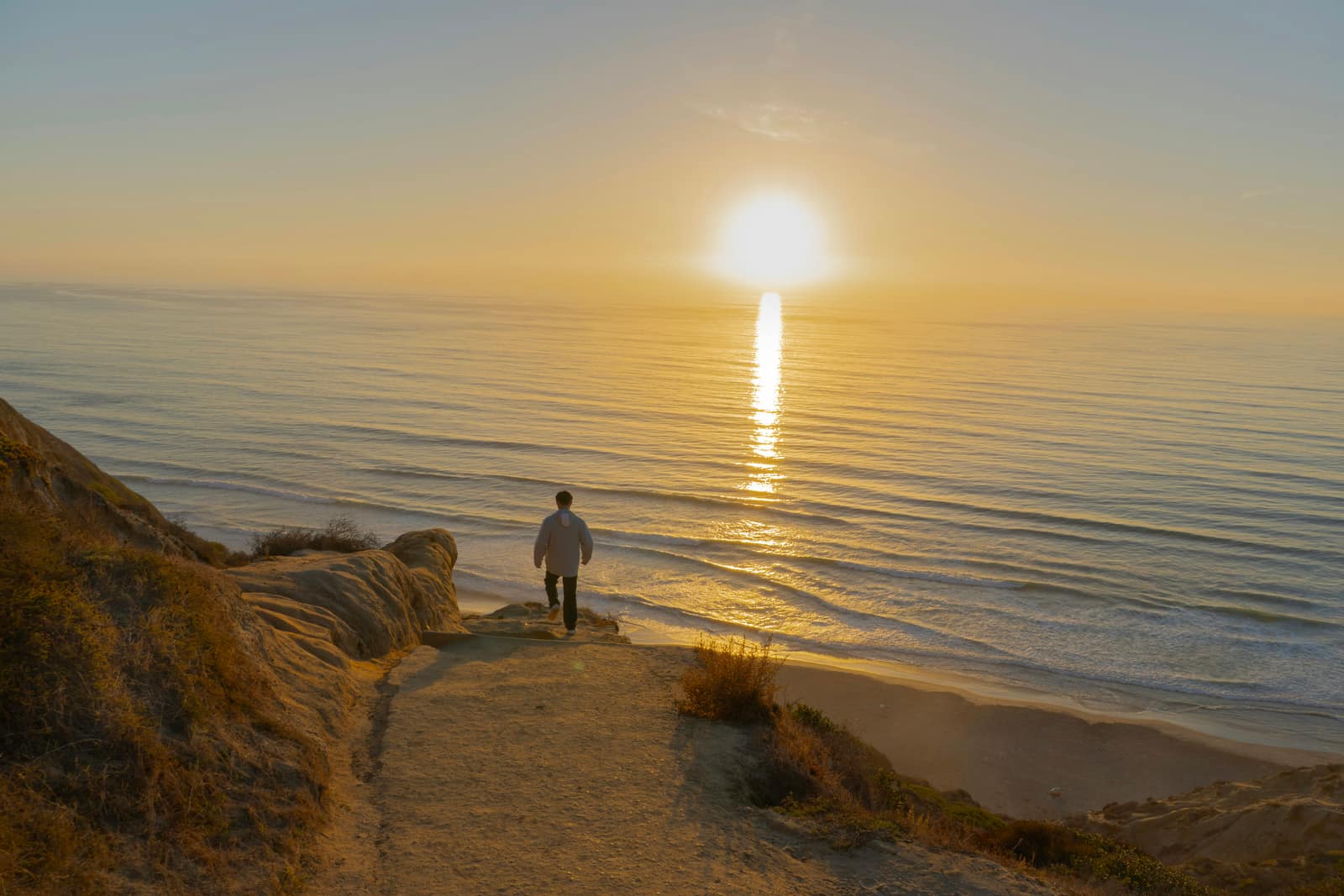 Man walks towards the ocean at sunset.